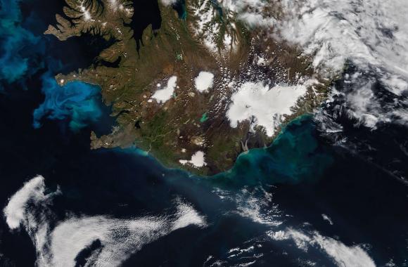 An aerial view of the Earth with colorful plankton blooms in the ocean off the coast of a landmass 
