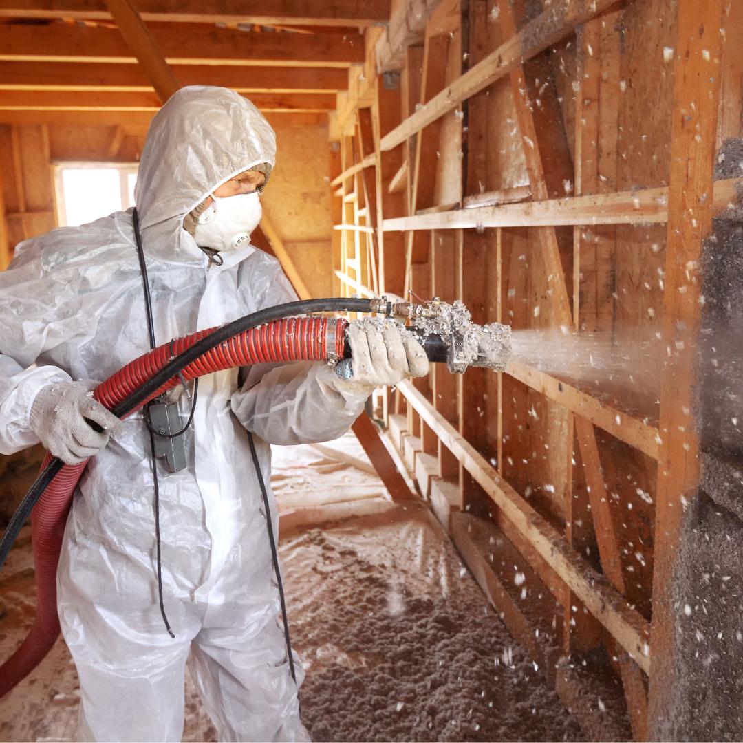 Worker sprays insulation in building frame.