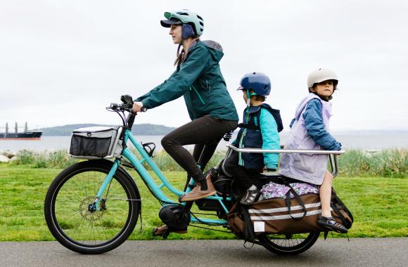 Parent riding electric bicycle with children seated in back carrier